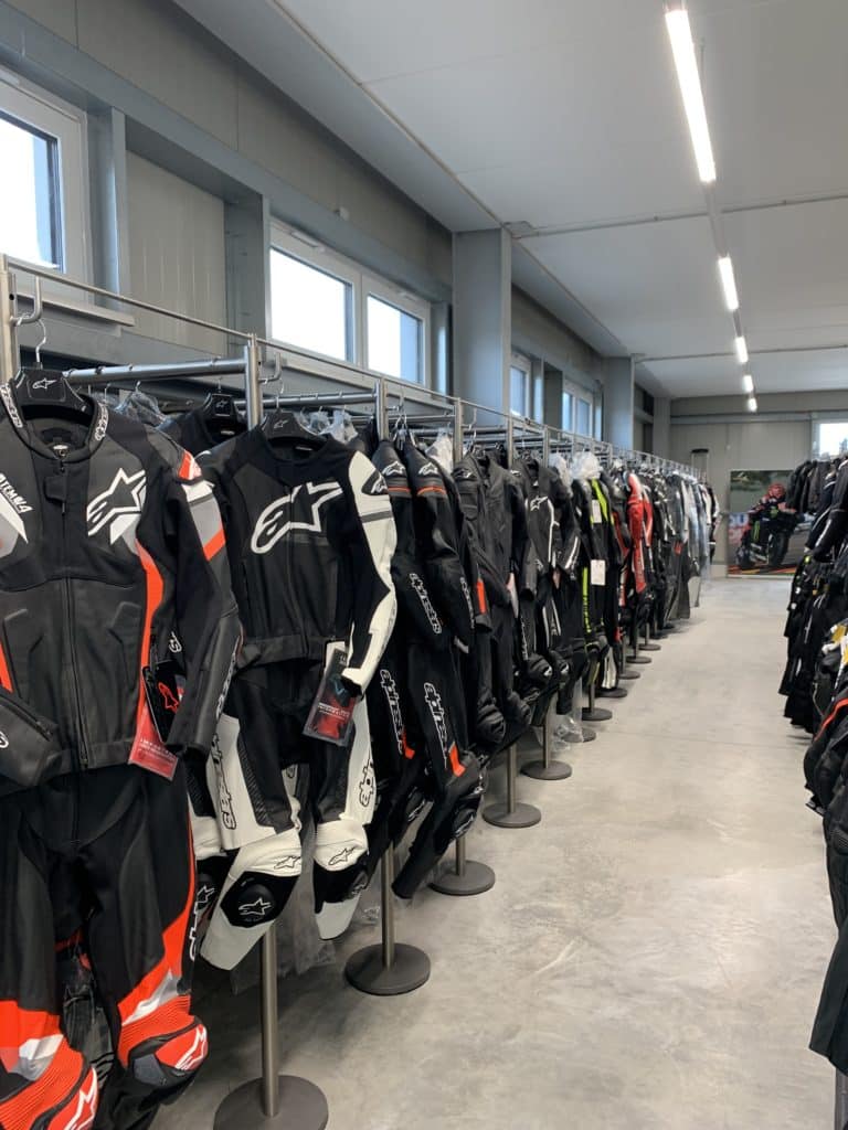 Ein Innenraum eines Motorradbekleidungsgeschäfts mit mehreren Reihen von Motorradanzügen auf Kleiderständern.
