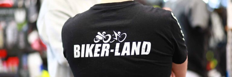 Ein Mann steht mit dem Rücken zur Kamera und trägt ein schwarzes T-Shirt mit dem Aufdruck „BIKER-LAND“.